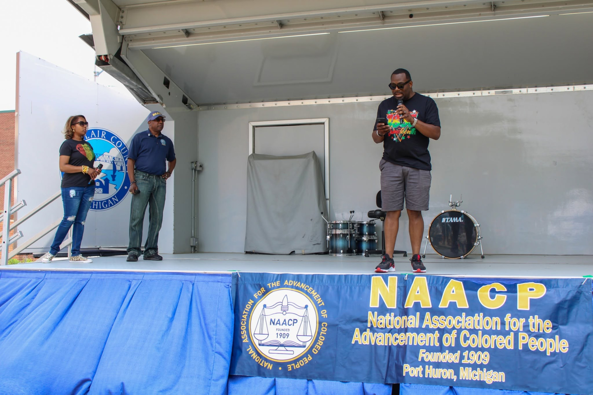 A host speaking on an outdoor stage at a community celebration
